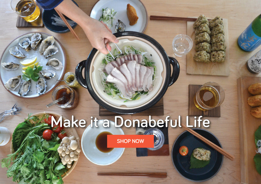 A dinner scene with steamed fish on the donabe. Oysters, veg, and rice balls surround the donabe.